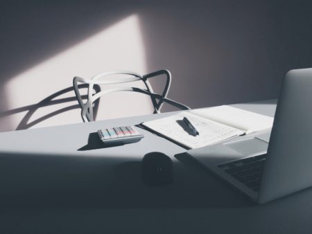 an empty chair in front of a notepad, calculator and laptop