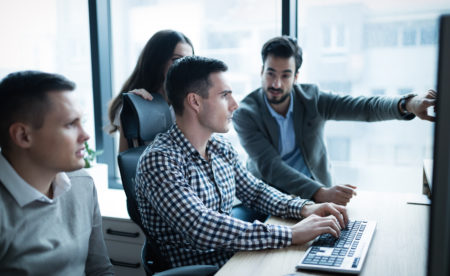 group of men and women working around a computer