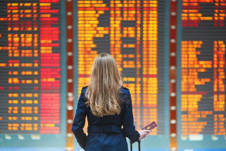 Woman's back whilst looking at a flight status board.