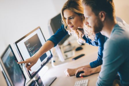 Man and woman in front of computer monitors looking at claims management software.