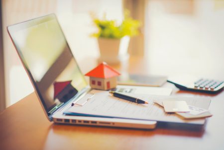 Documents and miniature house on top of an open laptop.