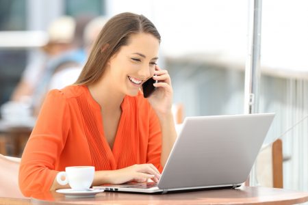 Happy customer in orange using a laptop and talking on phone while sitting