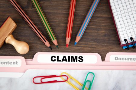 a folder labeled "claims" on top of table with pencils and paper clips