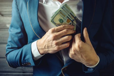 Man putting money from undisclosed commission inside his suit's pocket.