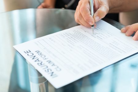Person's hand signing an insurance claim form.